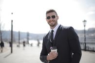 一位穿着西装、戴着墨镜的商人在户外拿着咖啡杯微笑