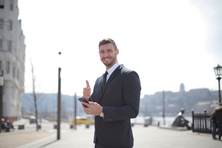 Man In Black Suit Jacket While Holding A Smartphone