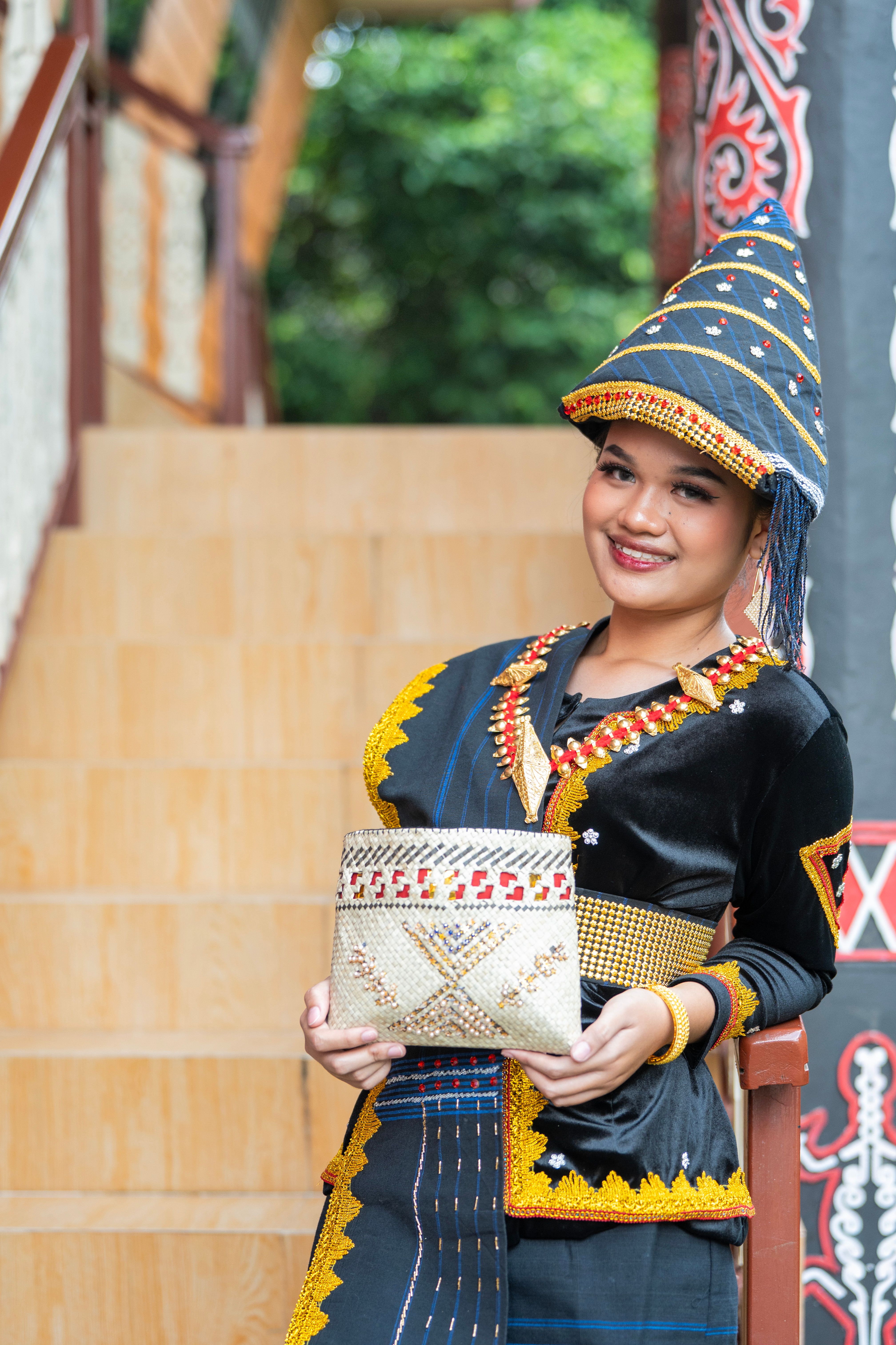 Gratuit Femme souriante vêtue d'une robe traditionnelle d'Asie du Sud-Est aux couleurs chatoyantes, tenant un sac artisanal. Photos