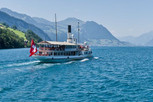 Free A scenic view of a historic paddle steamer cruising on Lake Lucerne with Swiss flag. Stock Photo