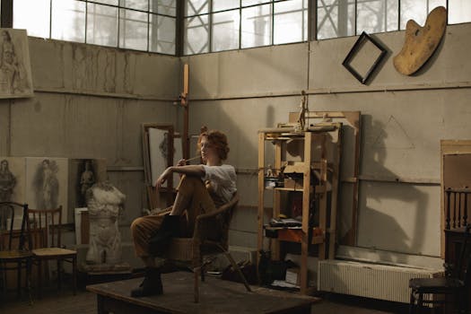 在充满草图和艺术材料的工业风格工作室中，艺术家坐在椅子上反思