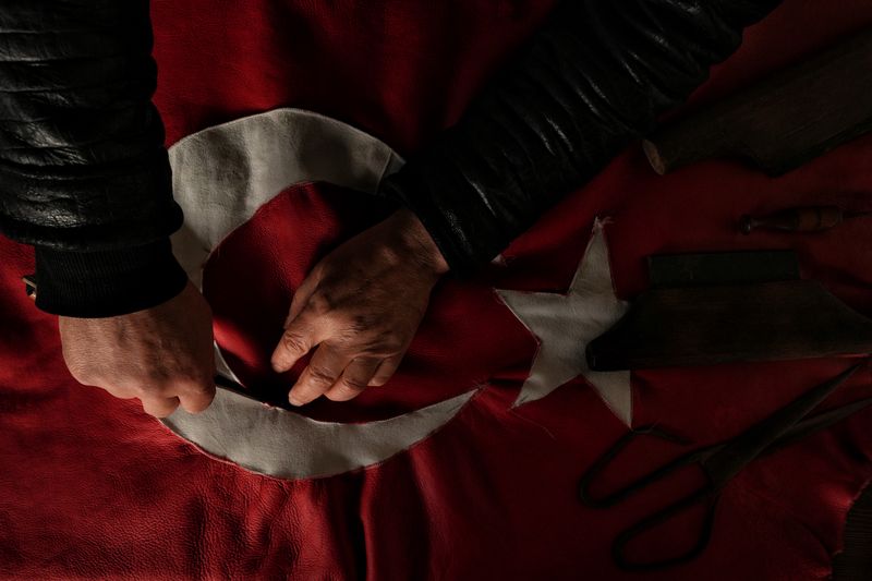 Close-up of a craftsman working on a leather Turkish flag with traditional tools.