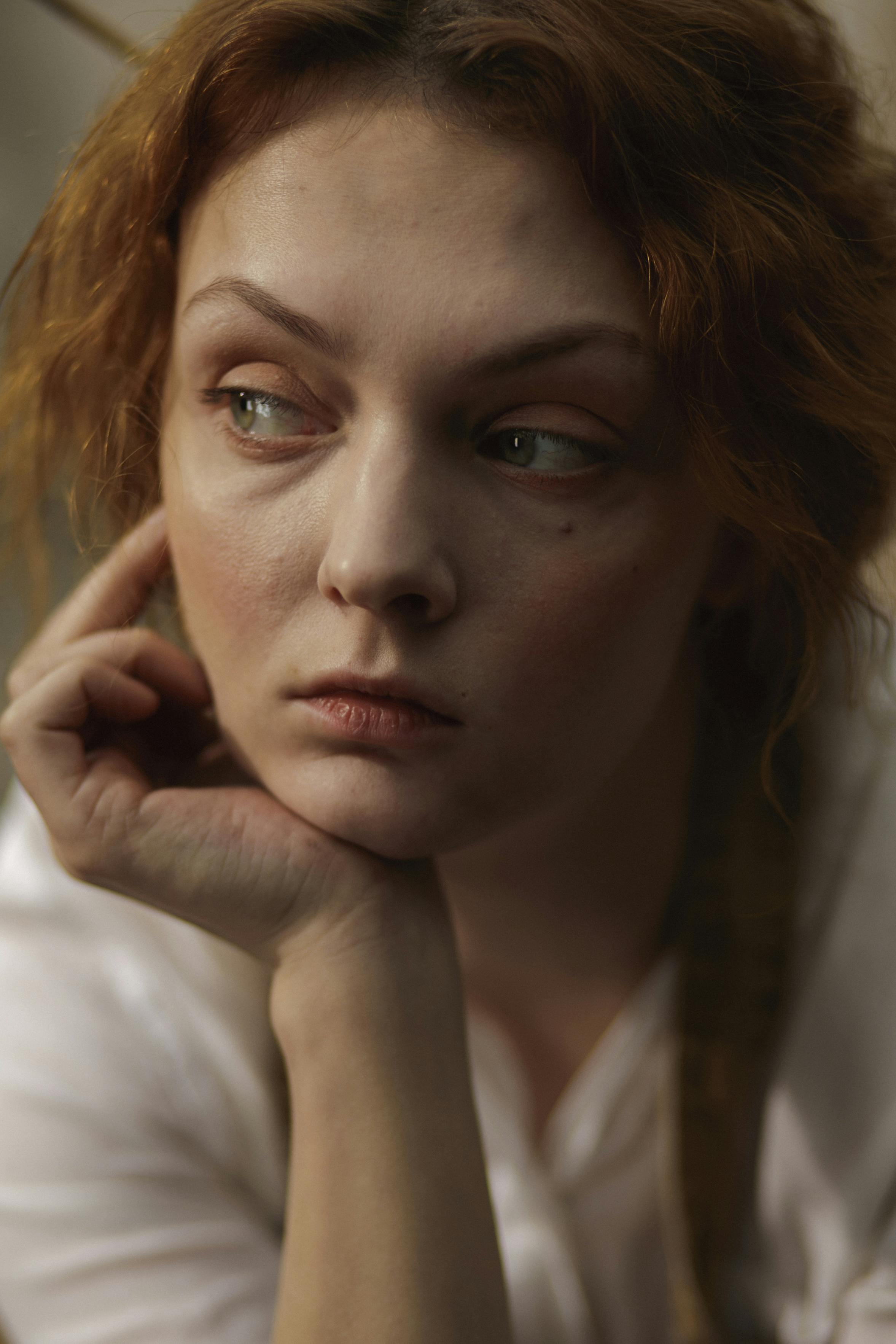 A close-up shot of a woman lost in thought with a pensive expression, her hand resting on her chin.