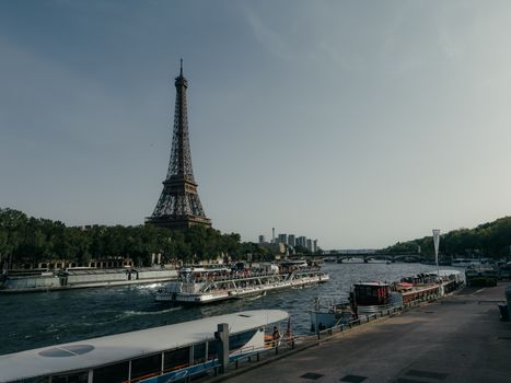 Iconic Eiffel Tower with boats on the Seine River in a bright, sunny day in Paris.