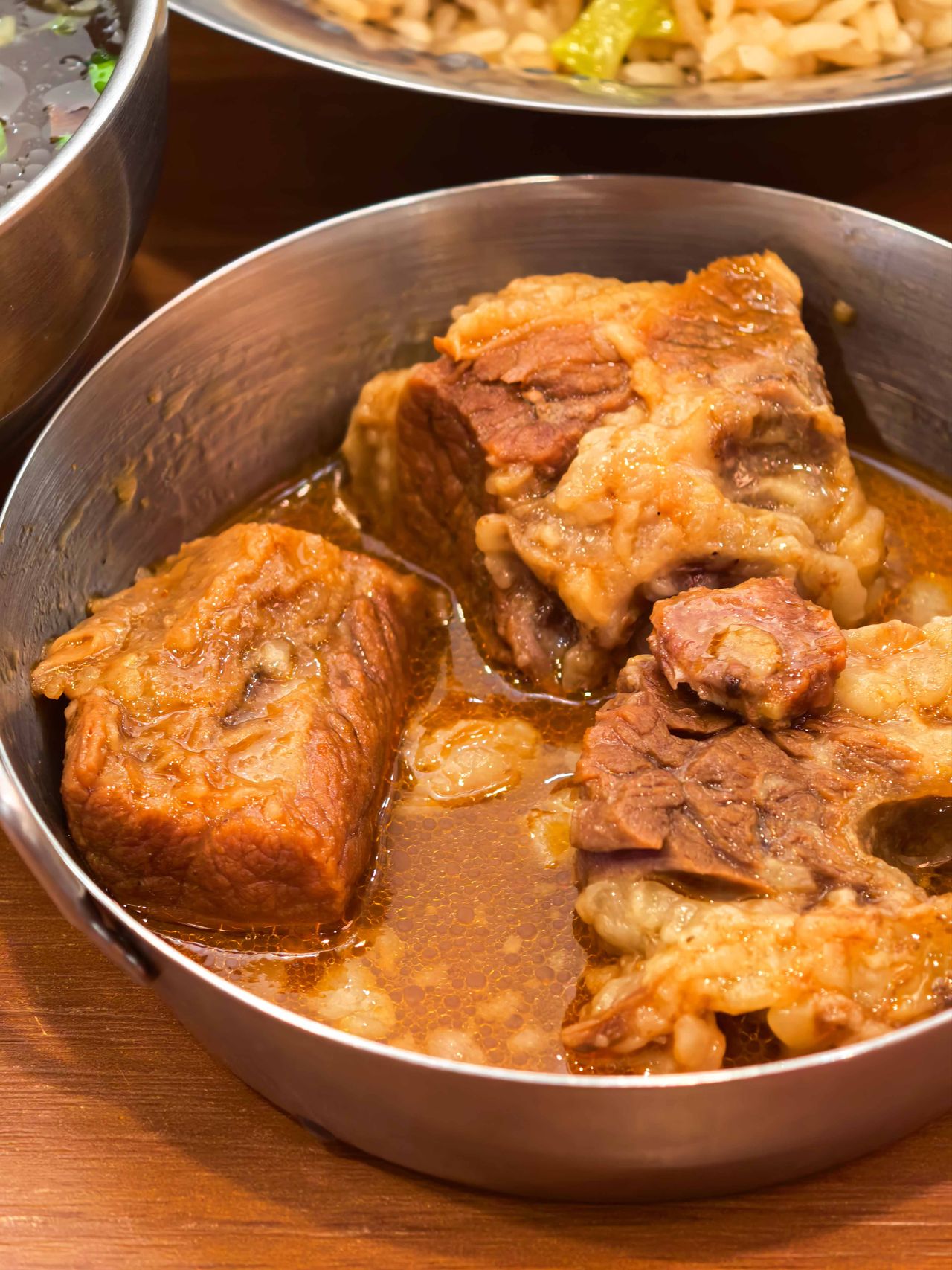 Chunks of braised beef in rich dark sauce served in a stainless steel bowl