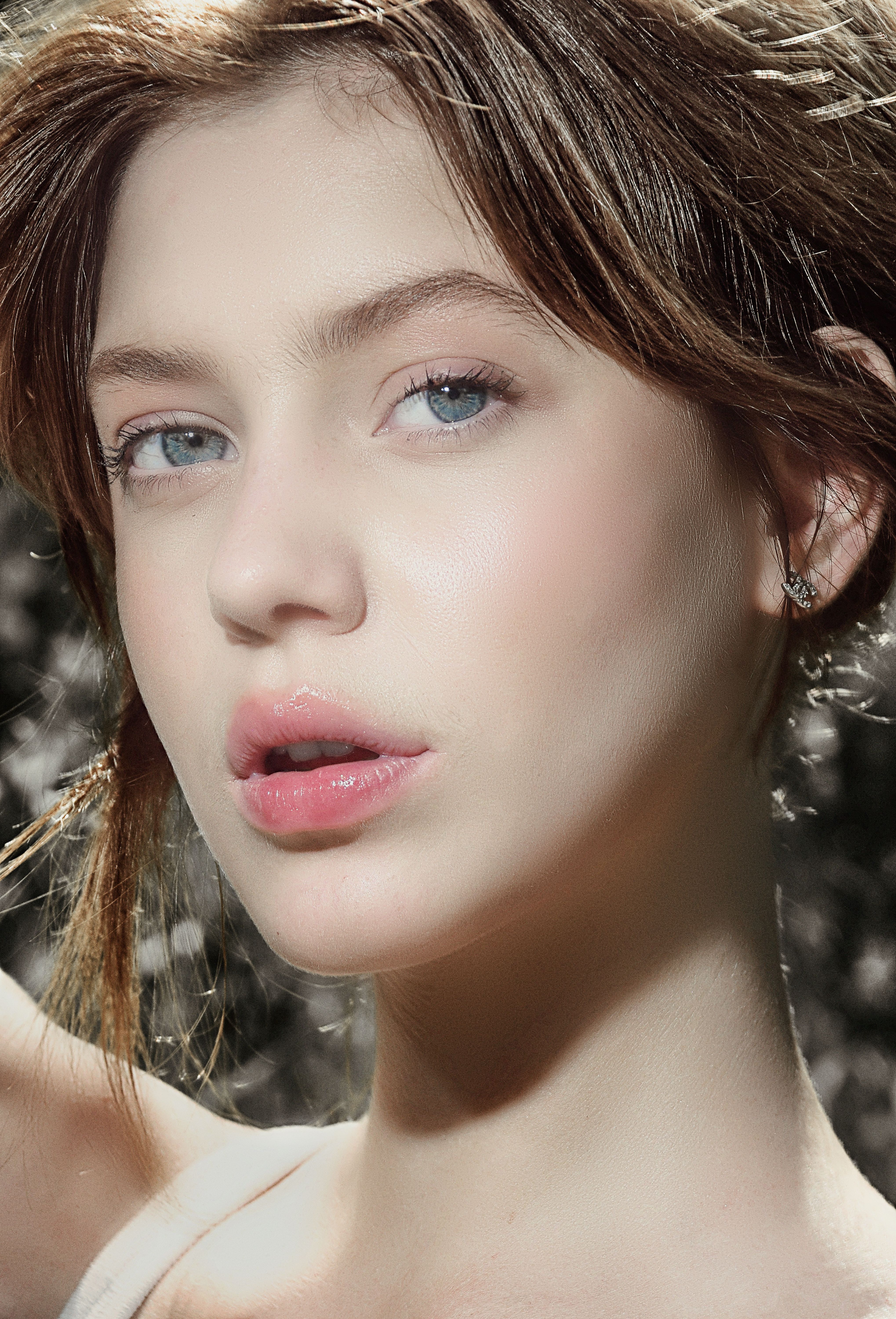 A soft-focus close-up of a young woman with natural makeup in sunlight.