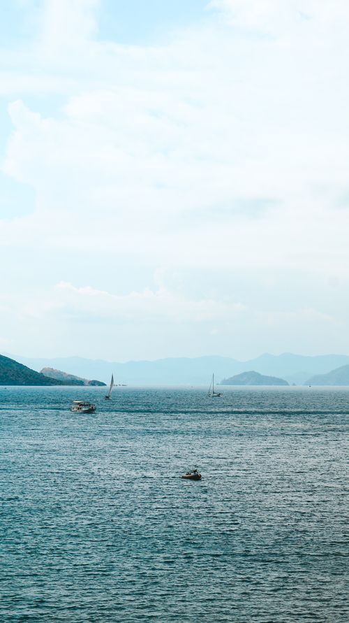 Free Peaceful seascape featuring sailboats, calm ocean, and distant islands under a bright sky. Stock Photo