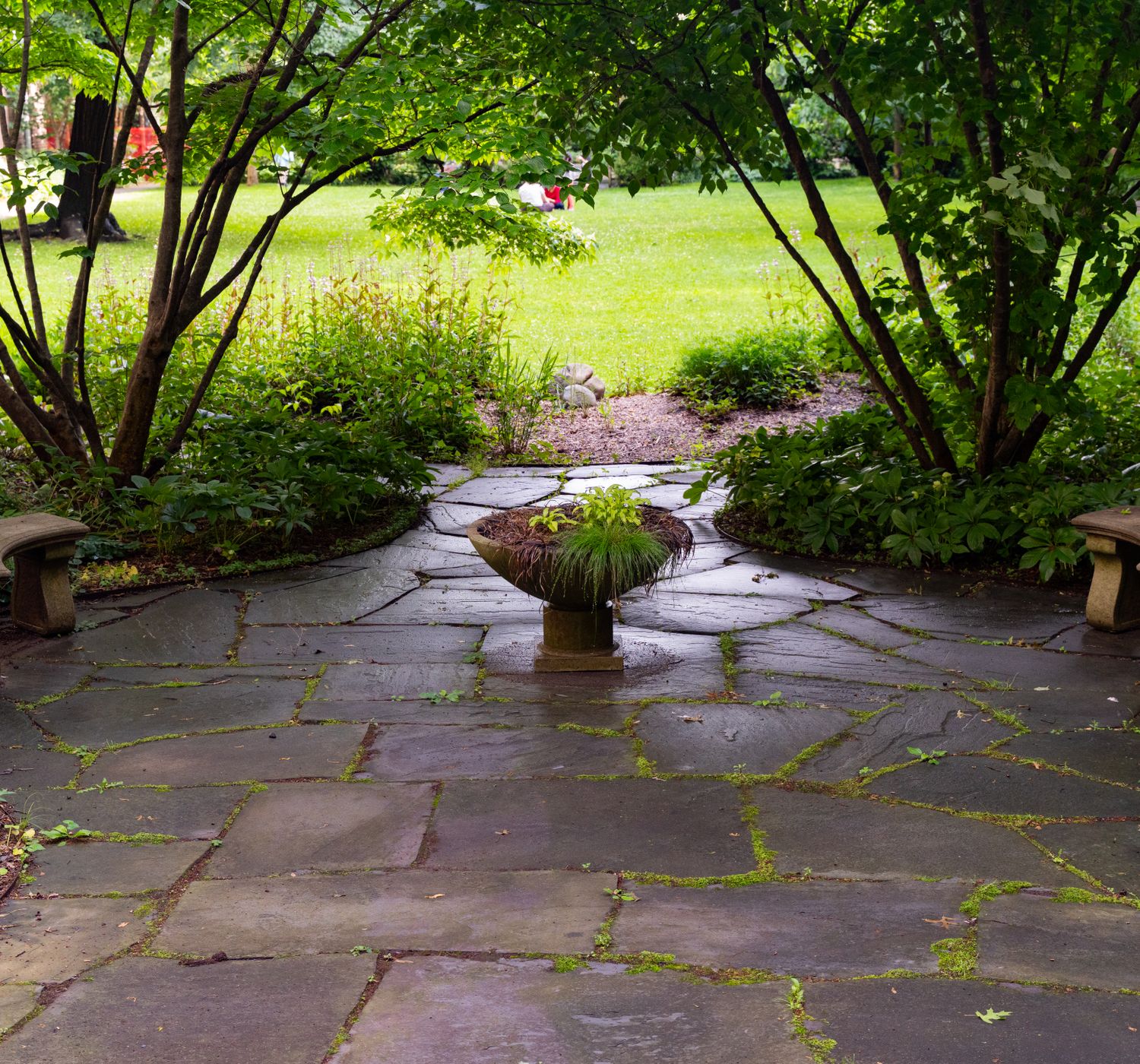 Peaceful stone patio surrounded by greenery and a central plant centerpiece in a New York garden.