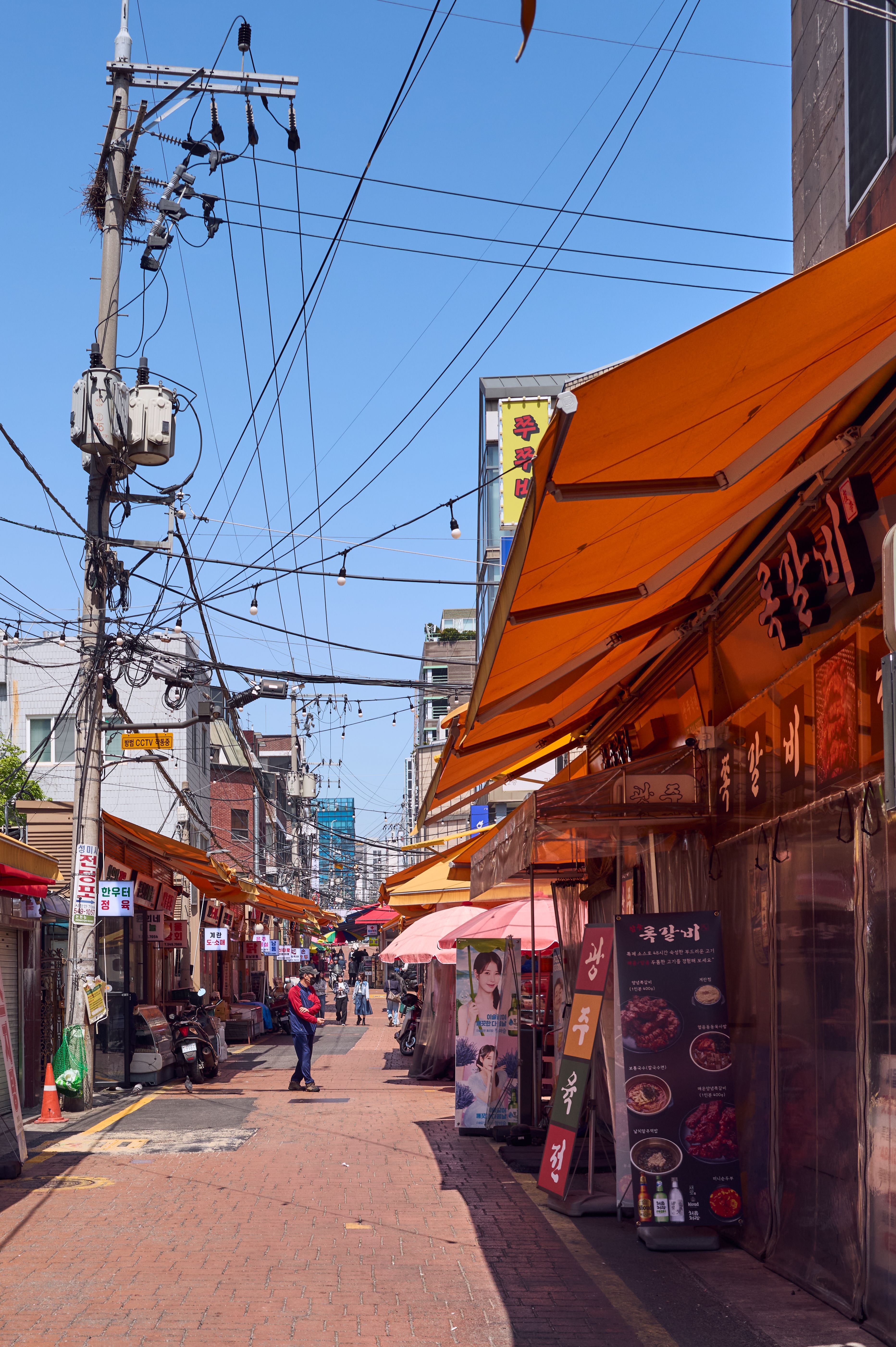 Explore a lively Korean street market bustling with colors, vendors, and food stalls under a bright blue sky.