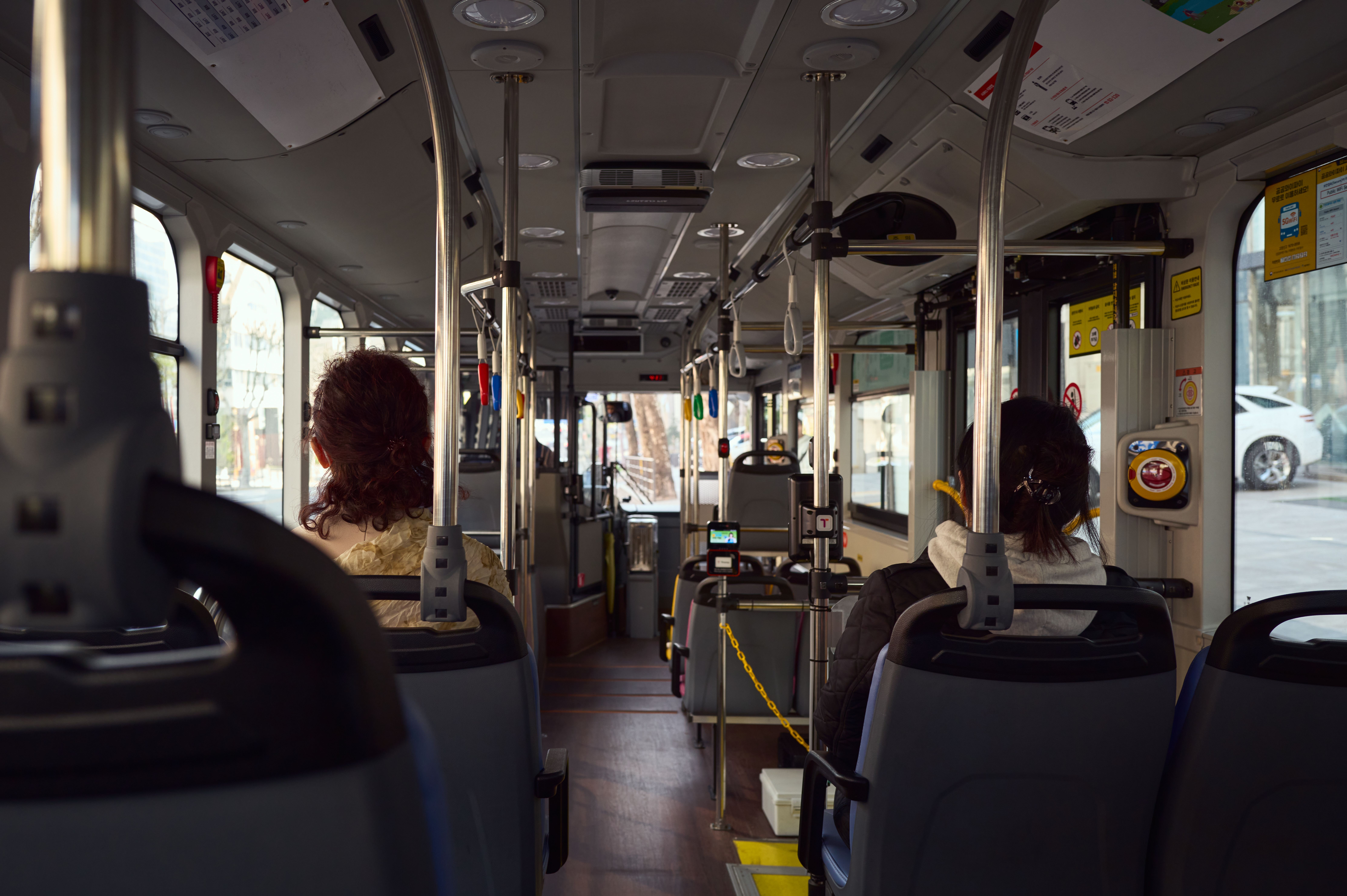 View of a public bus interior with seated passengers and visible city streets outside.