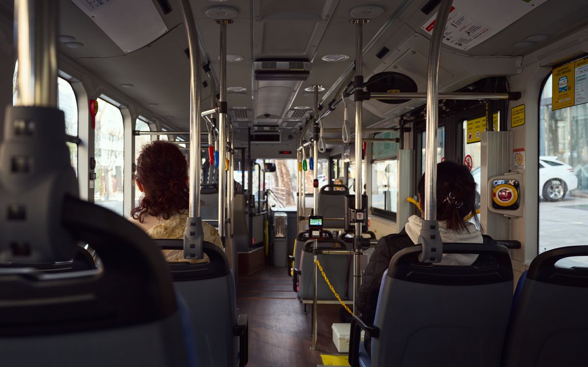 View of a public bus interior with seated passengers and visible city streets outside.
