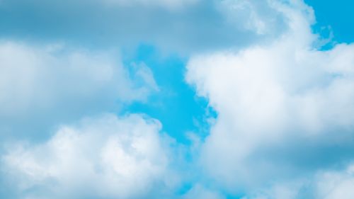 Free A serene view of fluffy white clouds in a bright blue sky, capturing a peaceful summer day. Stock Photo