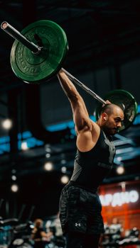 Adult male performing a barbell lift in a modern gym environment.