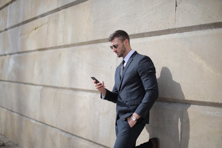 Man In Black Suit Jacket And Black Pants Standing By The Wall