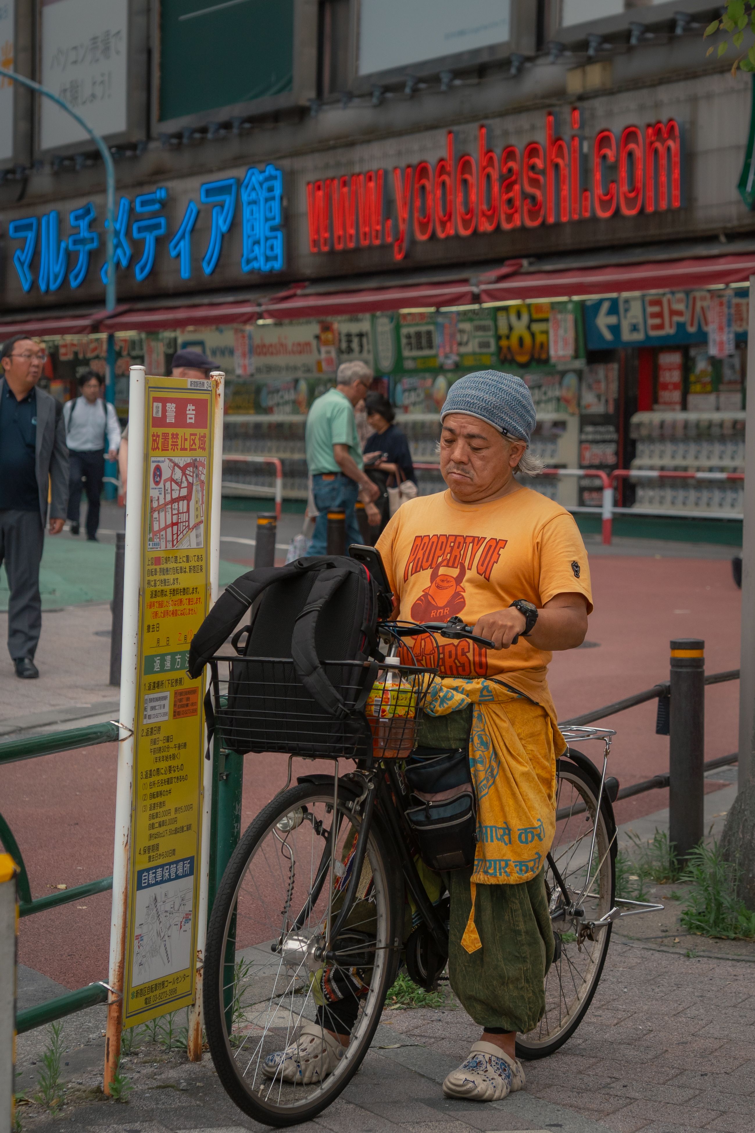 Local cyclist in Tokyo, Japan, next to Yodobashi Camera with vibrant city backdrop.