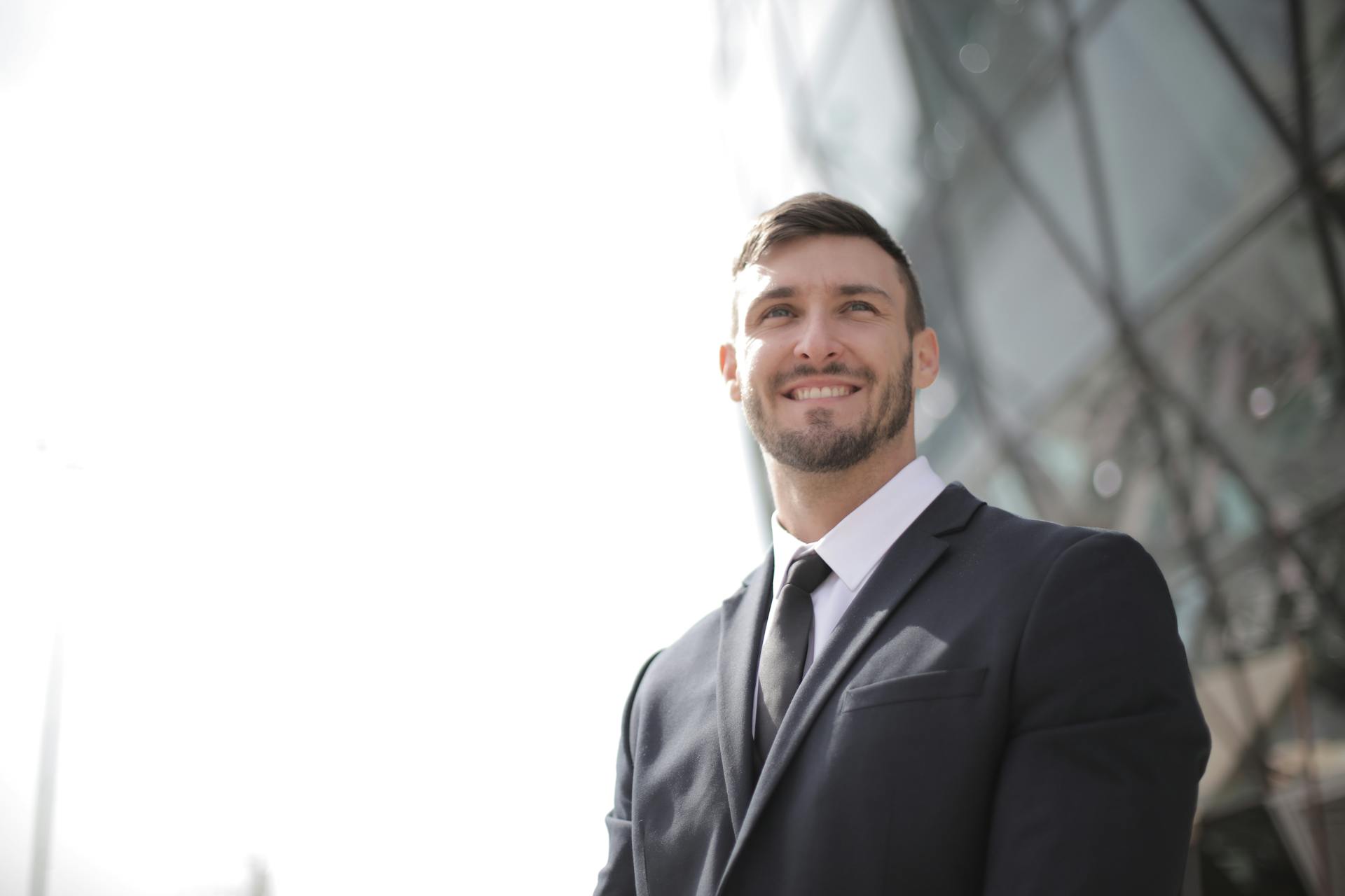 A happy businessman in a formal suit smiling confidently outdoors against a modern architectural backdrop.