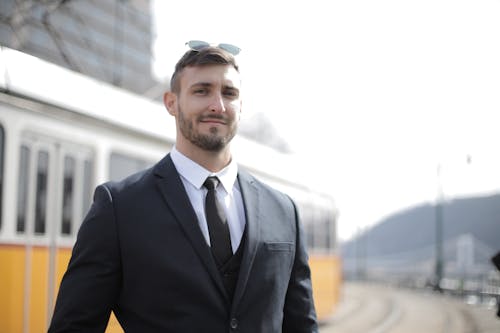 Confident businessman in a suit standing outdoors with sunglasses on a bright day.