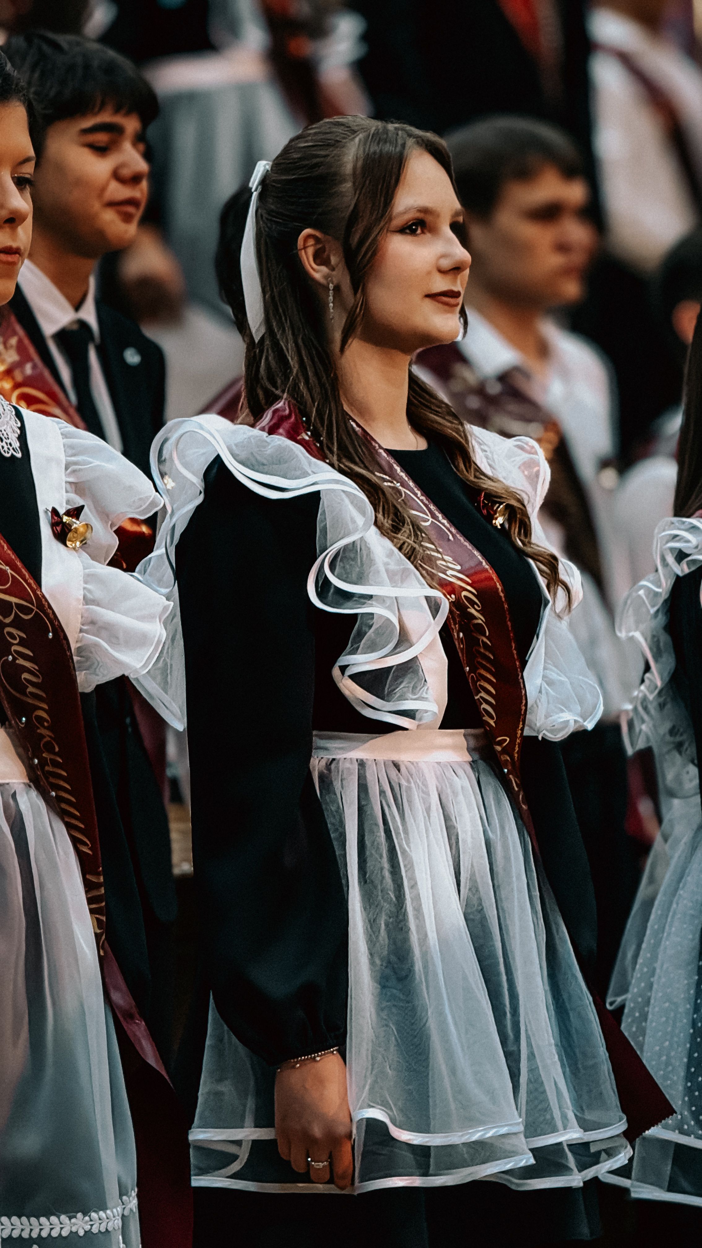 Students in traditional uniforms at a school graduation ceremony, standing in rows.