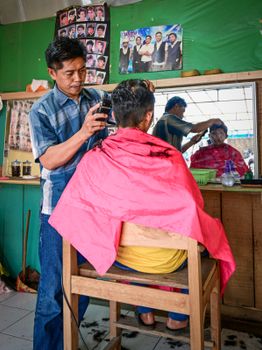 Barber cutting customer's hair in a traditional shop in Magelang, Indonesia.