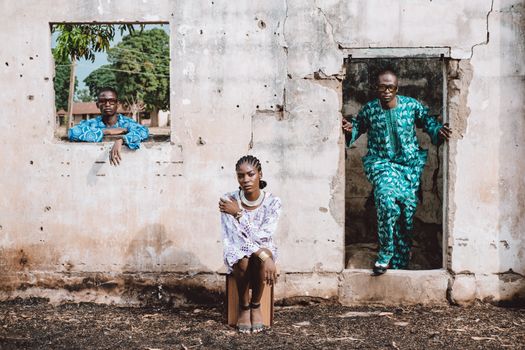 Three people in colorful traditional African attire pose against an old wall.