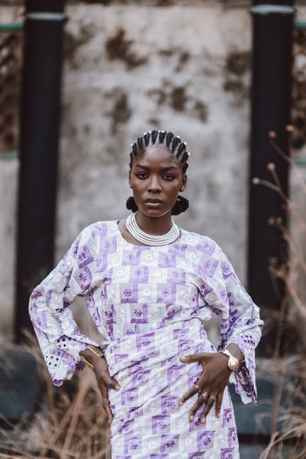 Confident woman in patterned African dress poses outdoors. Strong composition and vibrant style.