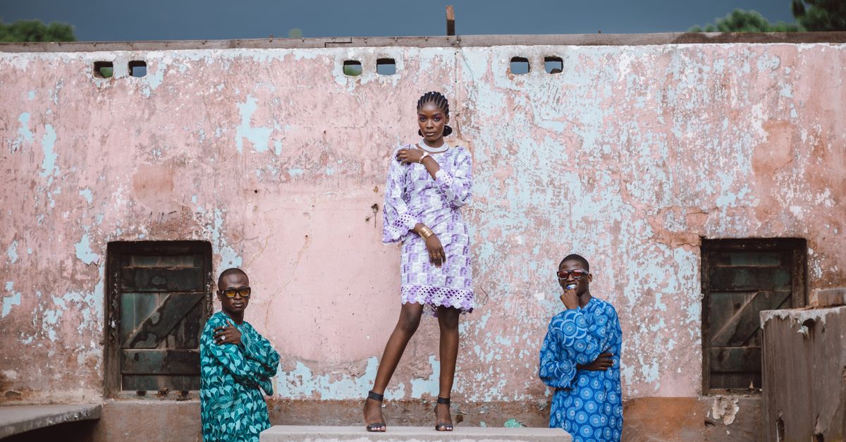 Young Ghanaian entrepreneur in Ho designing sportswear on a smartphone, colorful fabrics in background