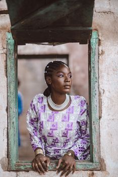 Portrait of a woman in traditional clothing gazing out an old rustic window frame.