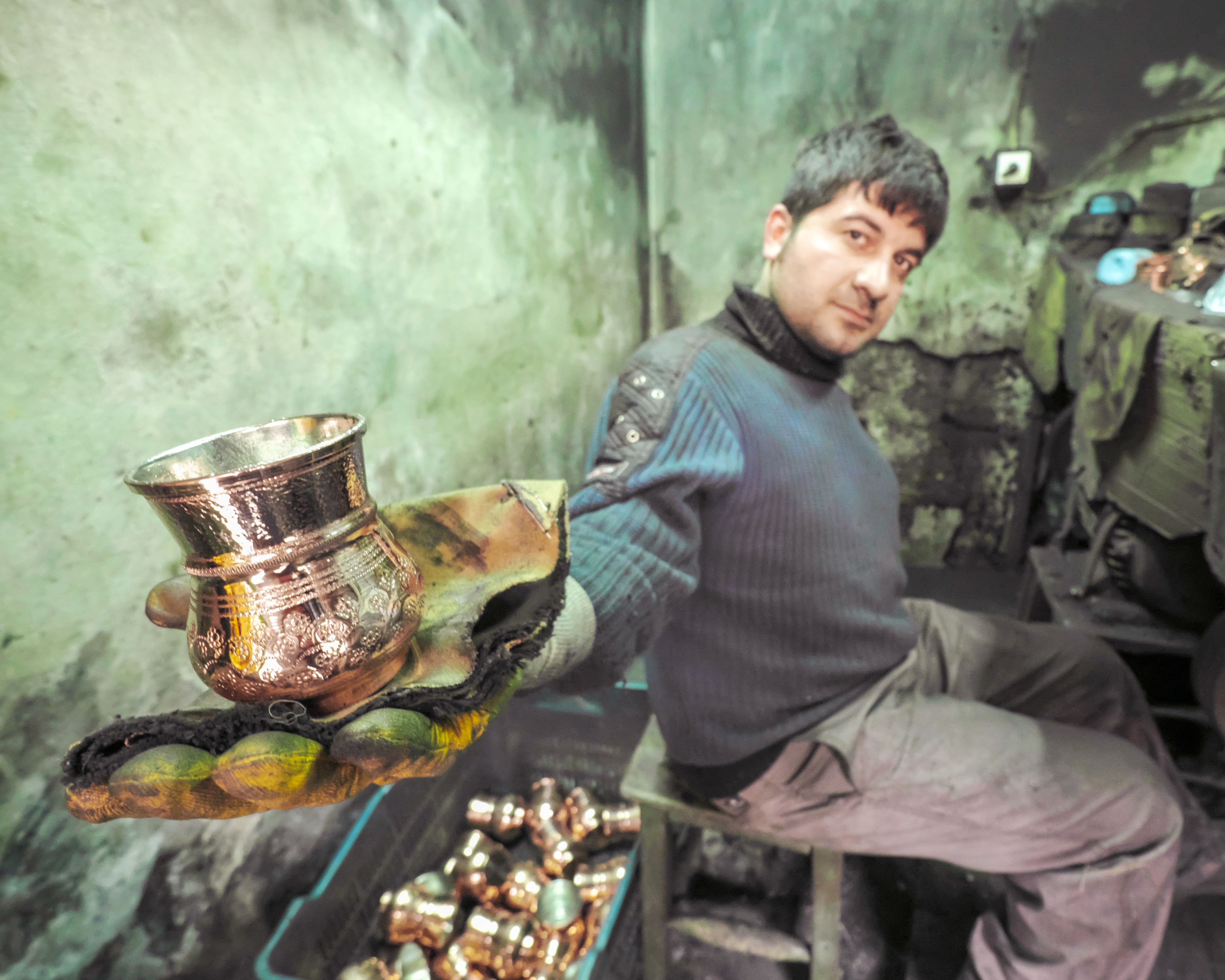 구리 시세 전망 관련 이미지 &mdash; Skilled craftsman showcasing intricate copper cup in a rustic workshop setting.