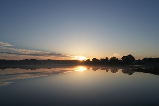 Captured at dawn, a tranquil sunrise reflected perfectly on a still lake horizon.