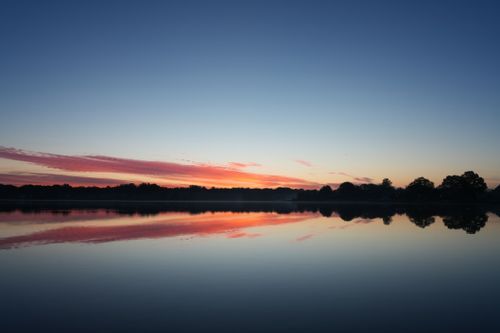Free Serene sunset over a calm lake with colorful reflections and silhouetted trees. Stock Photo