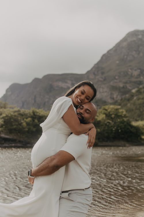 Free A loving couple shares a joyful embrace by a serene mountain lake, showcasing happiness and connection. Stock Photo
