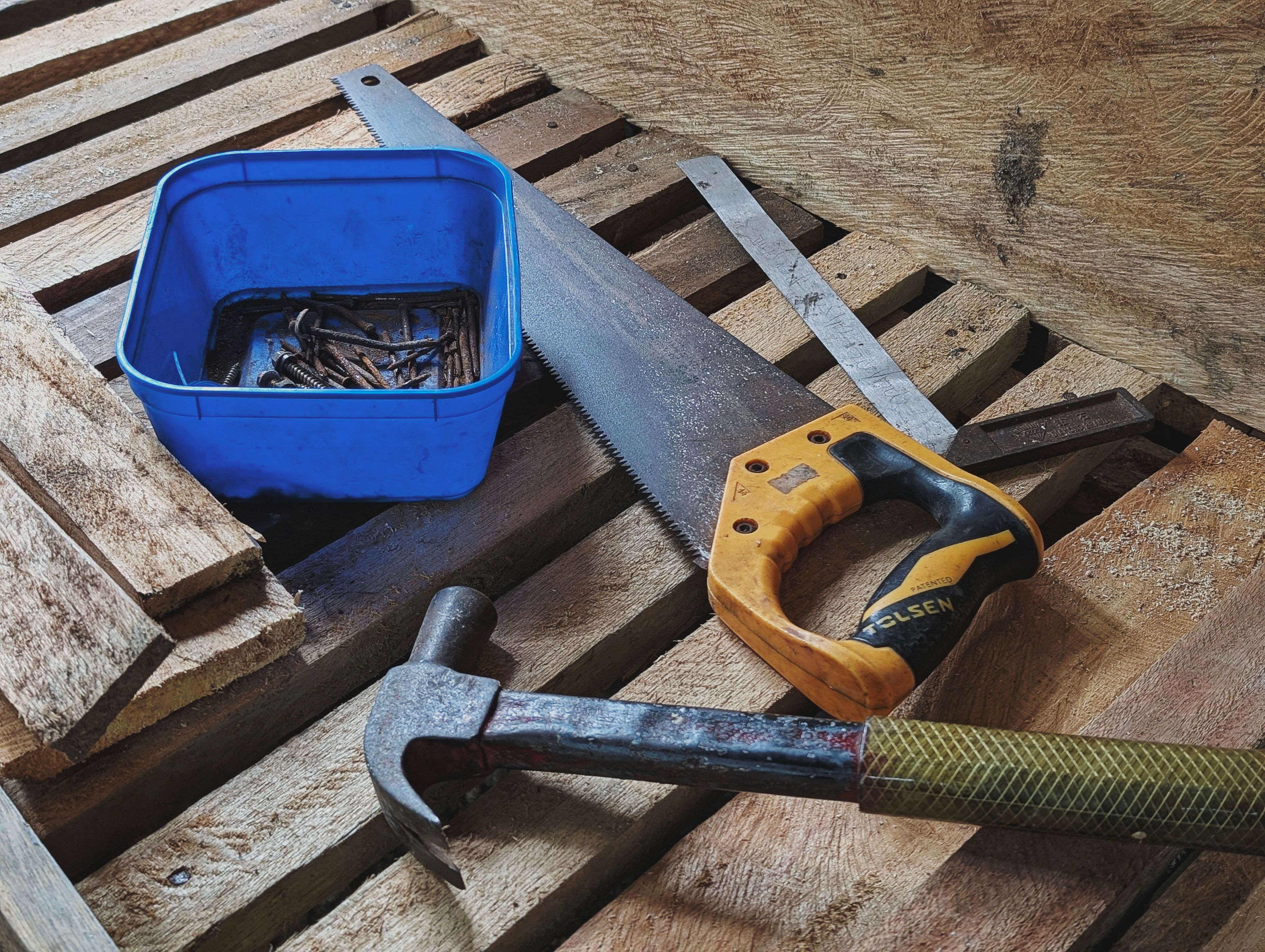 Handsaw, hammer, and blue toolbox on a wooden workbench outdoors