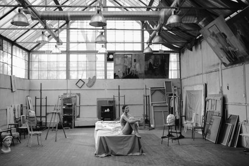 Free A nude woman posing in a sunlit art studio surrounded by easels and paintings. Stock Photo