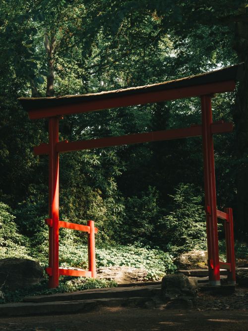 Free A tranquil red torii gate stands amidst a lush green garden, symbolizing transition in nature. Stock Photo
