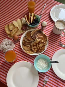 Inviting breakfast table with pancakes, fruit, and drinks on a striped tablecloth.