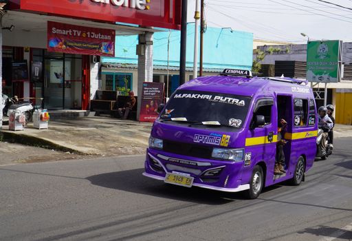 Vibrant purple public minibus drives on a busy street in West Java, Indonesia, showcasing local urban life.