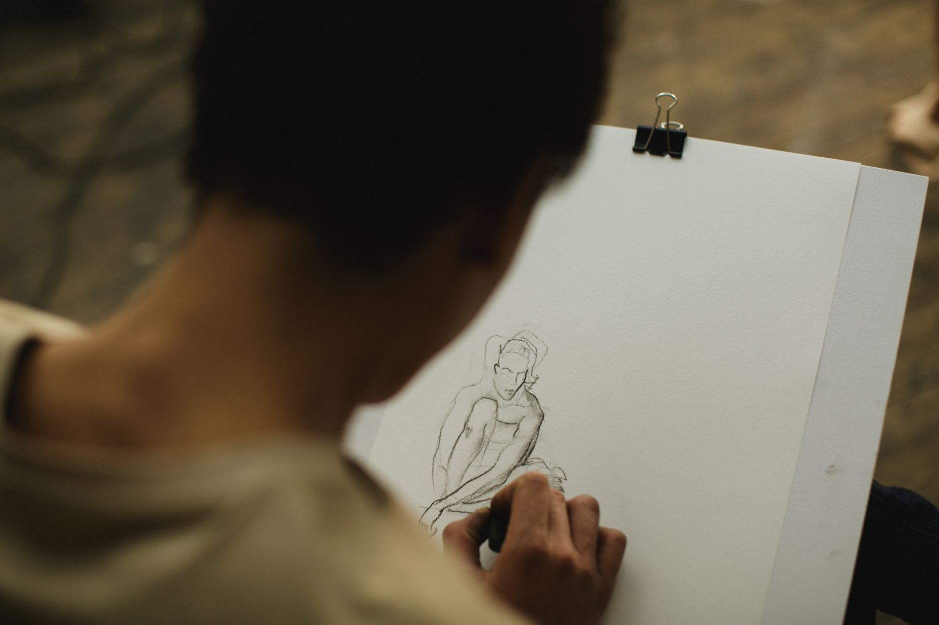 Focused artist sketching a seated figure on paper in a studio setting.