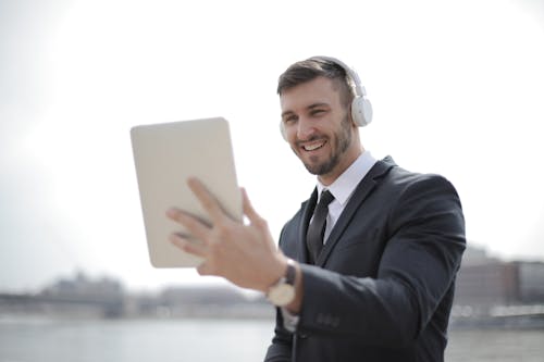 Man in Black Suit Jacket Holding a Tablet While Listening to Music