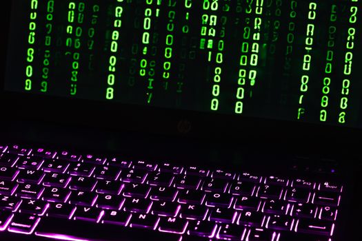 Illuminated laptop keyboard with Matrix-style green code cascading down screen.