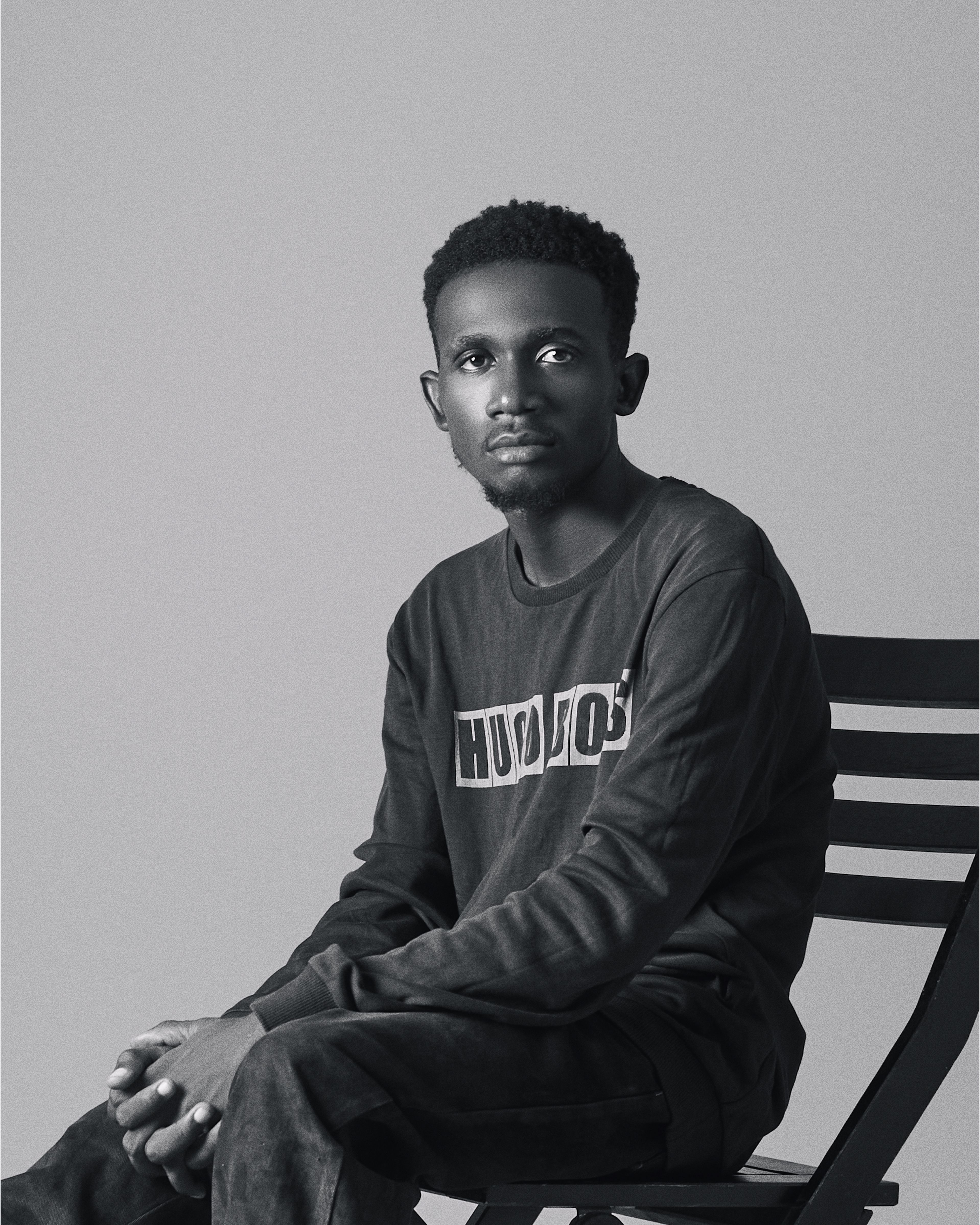Black and white portrait of an adult man sitting on a chair, expressing contemplation.