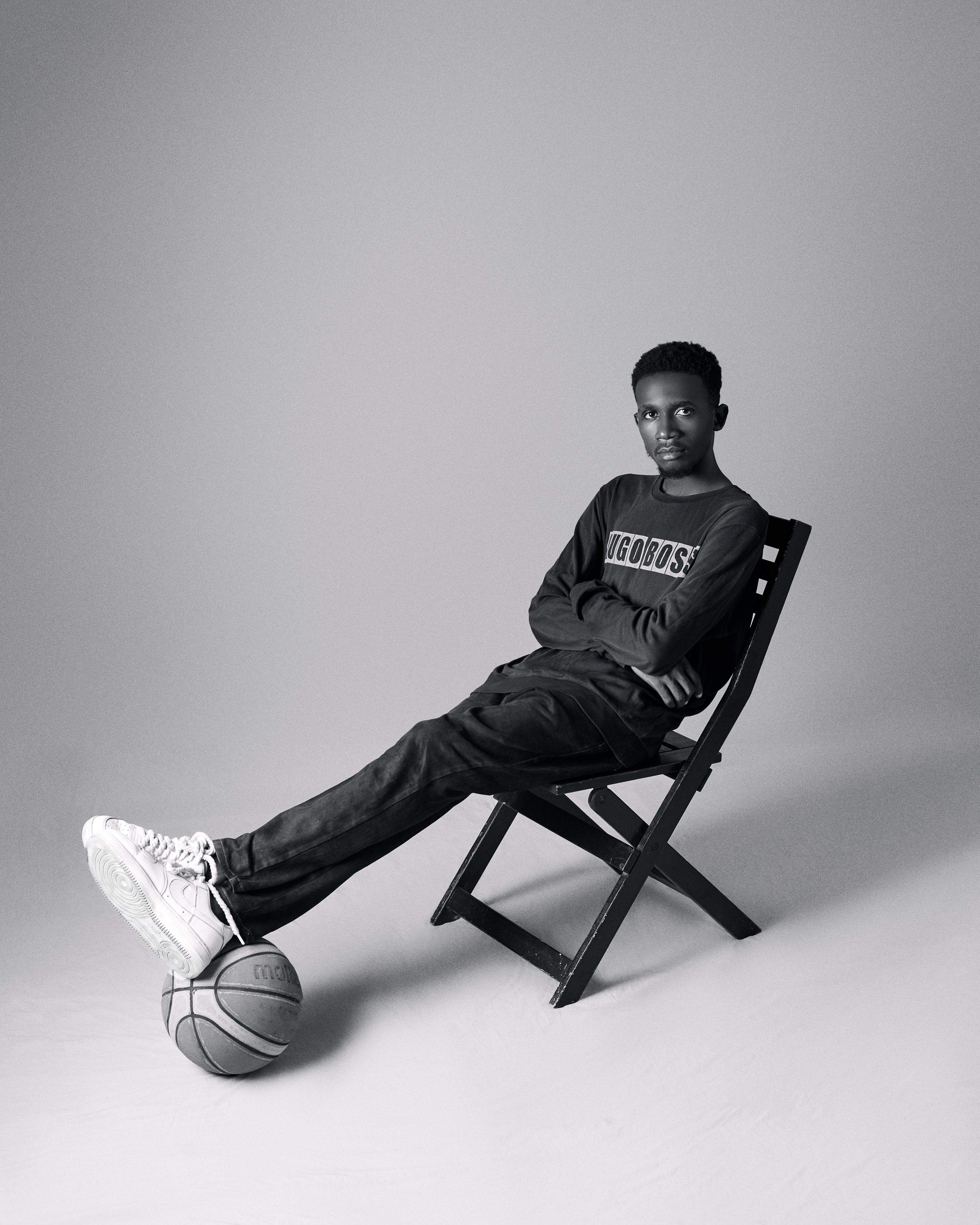 Black and white portrait of a teen seated with a basketball, wearing casual attire.