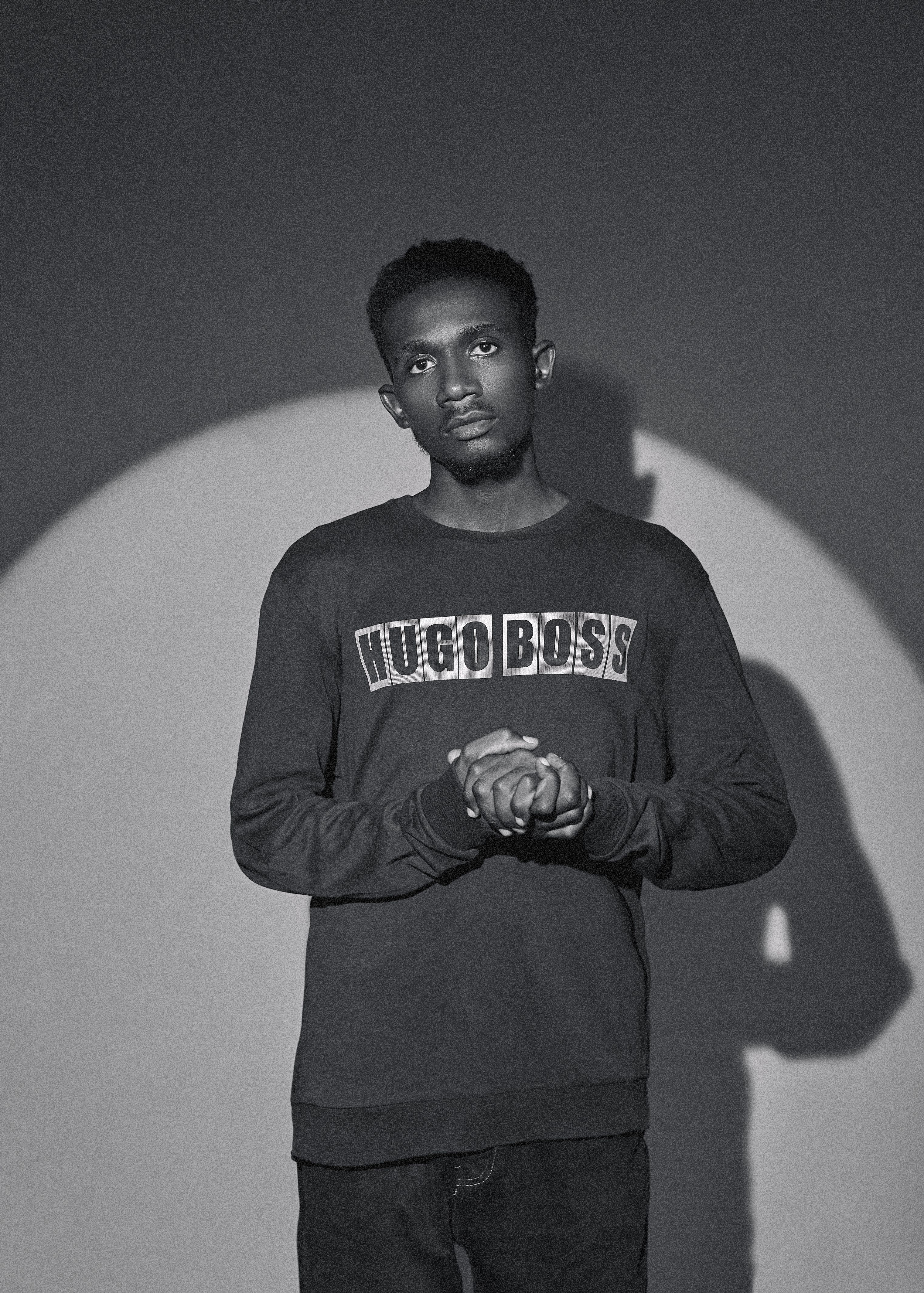 Monochrome photo of a man in casual wear standing in spotlight.
