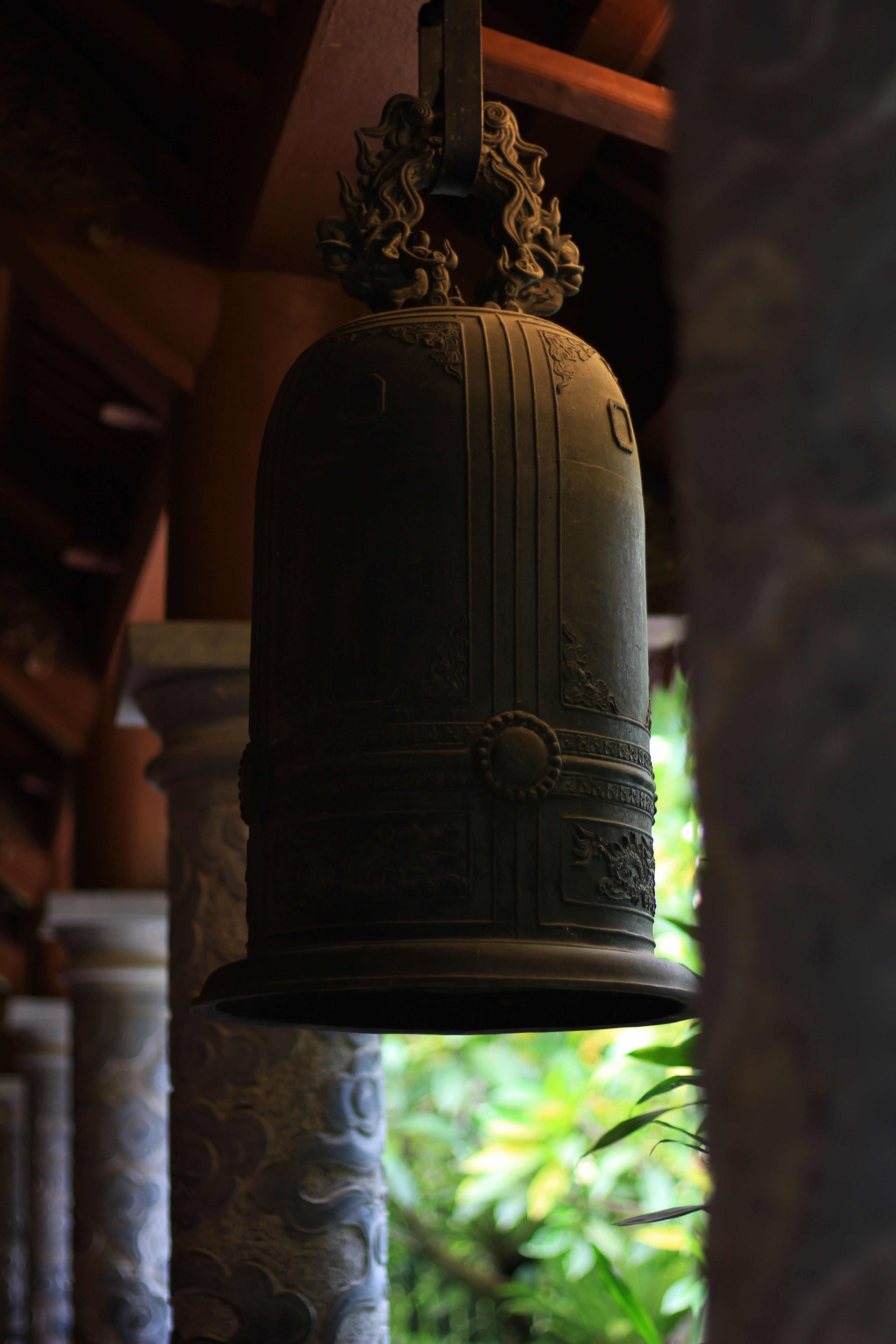 An ornate bronze temple bell hangs amid carved stone pillars, exuding a serene atmosphere.
