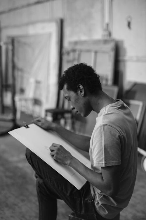 Grayscale Photo Of A Man Sketching On White Cardboard