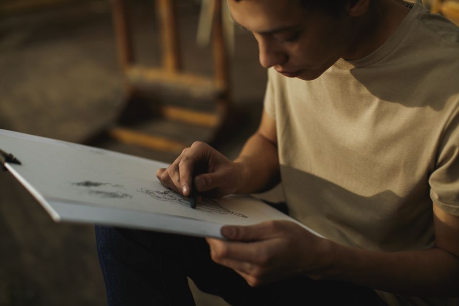 Focused adult drawing with charcoal on paper in an indoor art studio setting.