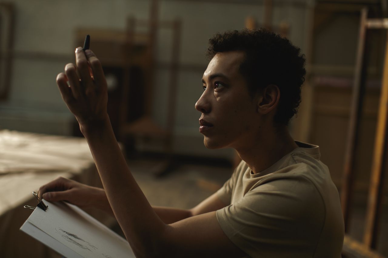 side profile of a focused artist sketching indoors in dim lighting