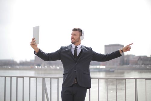 Free Businessman in formal attire using a tablet for a video call while standing by a river. Stock Photo