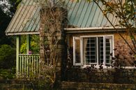 Rustic cottage with open windows and lush garden in a serene setting.