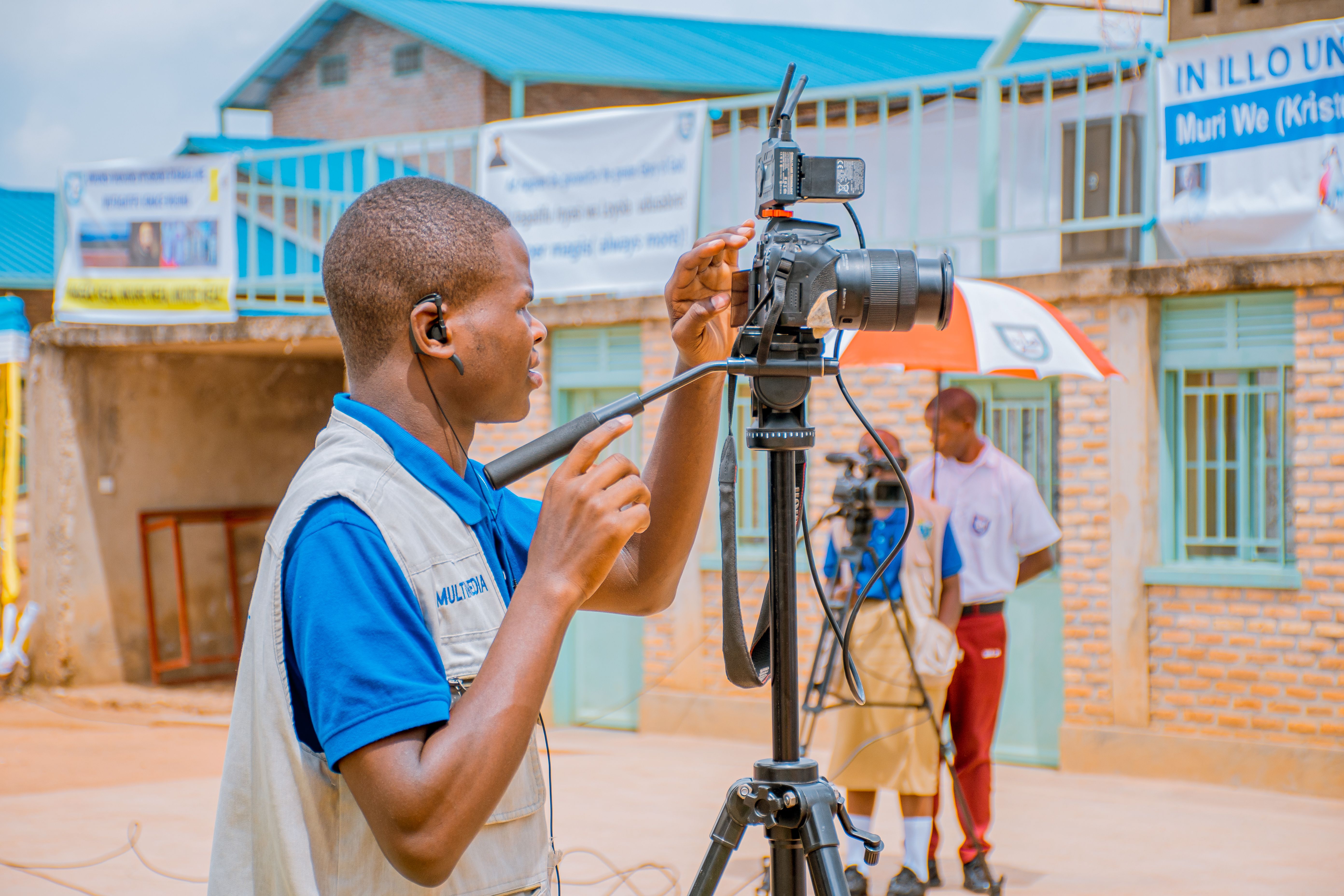 A professional cameraman adjusts his camera setup outdoors, preparing for a shoot under sunny skies.