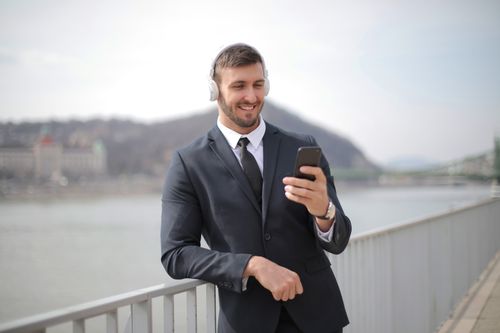 Free Smiling businessman in a suit listens to music on smartphone by a river. Stock Photo